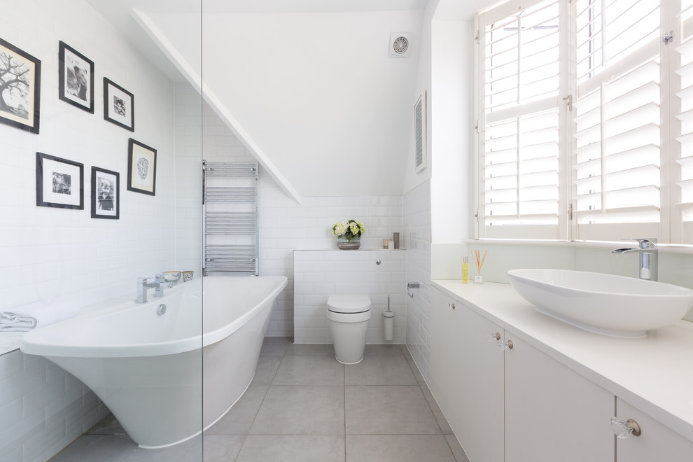 This is an example of a medium sized contemporary bathroom in London with a freestanding bath, white walls, a vessel sink, flat-panel cabinets, white cabinets, a one-piece toilet, white tiles and metro tiles.