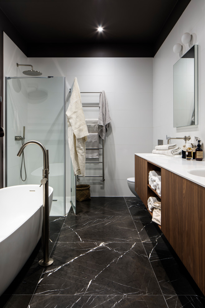 Large trendy master porcelain tile and black floor bathroom photo in London with flat-panel cabinets, medium tone wood cabinets, white walls, an integrated sink, a hinged shower door and white countertops