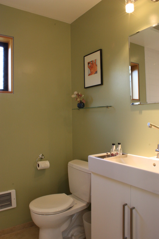 Modelo de cuarto de baño moderno pequeño con lavabo integrado, armarios con paneles lisos, puertas de armario blancas, encimera de acrílico, ducha empotrada, sanitario de dos piezas, paredes verdes, suelo de travertino y aseo y ducha