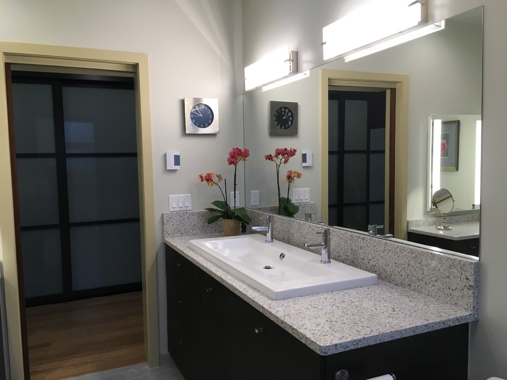 Modern inredning av ett mellanstort en-suite badrum, med släta luckor, svarta skåp, en toalettstol med separat cisternkåpa, grå väggar, klinkergolv i keramik, ett avlångt handfat, granitbänkskiva och grått golv