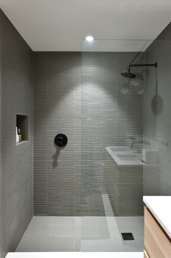 На фото: ванная комната среднего размера в стиле модернизм с плоскими фасадами, светлыми деревянными фасадами, душем в нише, раздельным унитазом, серой плиткой, керамогранитной плиткой, серыми стенами, полом из керамогранита, душевой кабиной, врезной раковиной, столешницей из искусственного камня, белым полом и открытым душем