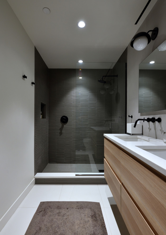 Пример оригинального дизайна: ванная комната среднего размера: освещение в стиле модернизм с плоскими фасадами, светлыми деревянными фасадами, душем в нише, раздельным унитазом, серой плиткой, керамогранитной плиткой, серыми стенами, полом из керамогранита, душевой кабиной, врезной раковиной, столешницей из искусственного камня, белым полом и открытым душем
