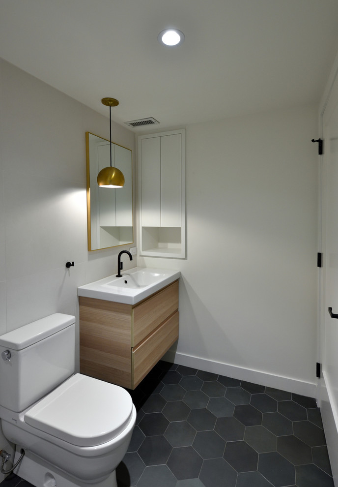 Medium sized contemporary shower room bathroom in New York with flat-panel cabinets, light wood cabinets, an alcove bath, a shower/bath combination, a one-piece toilet, white tiles, porcelain tiles, white walls, ceramic flooring, an integrated sink, solid surface worktops, black floors and a shower curtain.