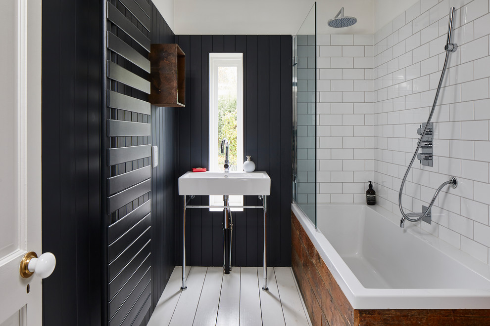 Photo of a contemporary ensuite bathroom in London with a built-in bath, a shower/bath combination, white tiles, metro tiles, black walls, painted wood flooring, a console sink and white floors.