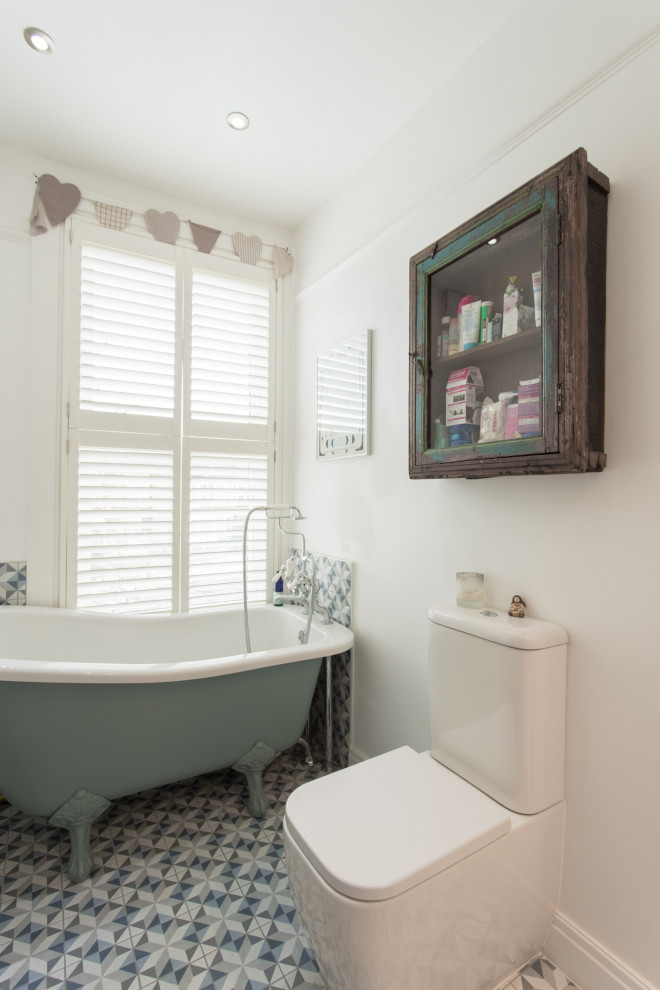 Immagine di una stanza da bagno industriale con vasca con piedi a zampa di leone, WC a due pezzi, pareti bianche e pavimento multicolore