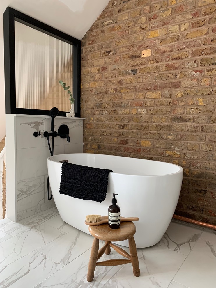 Industriell inredning av ett litet en-suite badrum, med ett fristående badkar, en toalettstol med hel cisternkåpa, vit kakel, porslinskakel, bruna väggar, klinkergolv i porslin och vitt golv