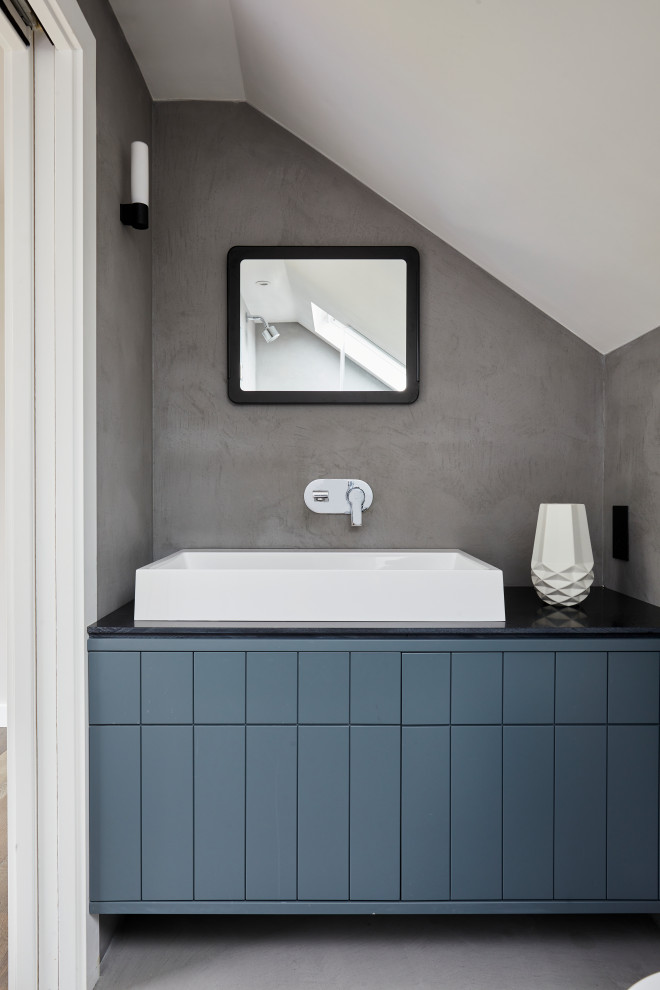 На фото: ванная комната в современном стиле с плоскими фасадами, синими фасадами, серыми стенами, настольной раковиной, серым полом и черной столешницей с