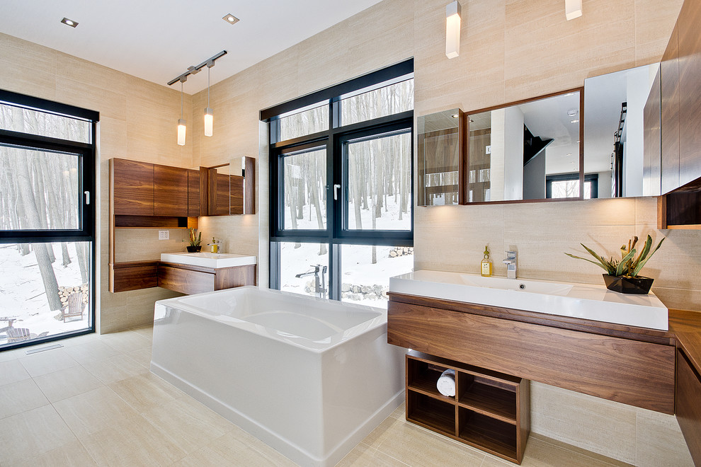 Modernes Badezimmer mit integriertem Waschbecken, flächenbündigen Schrankfronten, hellbraunen Holzschränken, freistehender Badewanne, beigen Fliesen und beigem Boden in Montreal