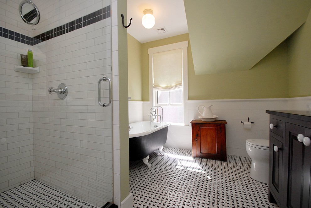 Inredning av ett lantligt badrum, med luckor med profilerade fronter, ett badkar med tassar, en dubbeldusch, svart och vit kakel, keramikplattor, gröna väggar och bänkskiva i täljsten
