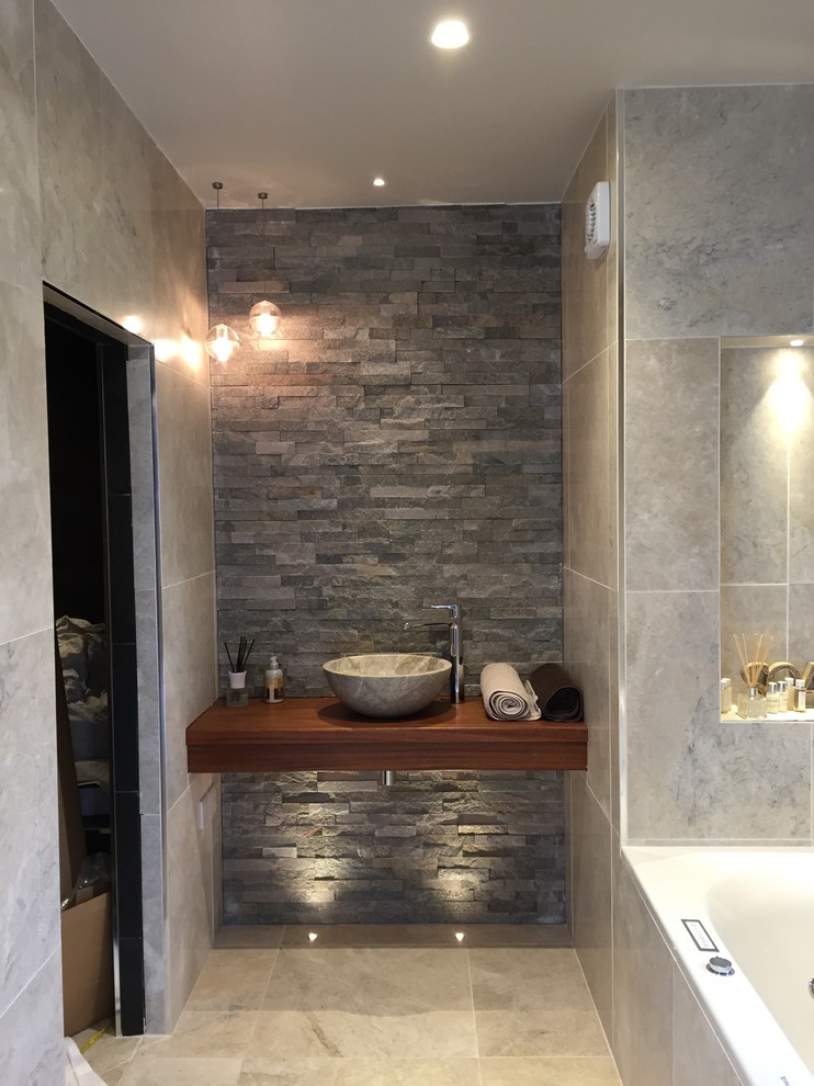 Idéer för mellanstora funkis badrum, med ett konsol handfat, ett platsbyggt badkar, en kantlös dusch, stenkakel, kalkstensgolv, träbänkskiva och grå kakel