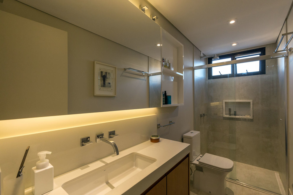 Photo of a small contemporary shower room bathroom in Other with flat-panel cabinets, medium wood cabinets, a one-piece toilet, grey tiles, porcelain tiles, grey walls, porcelain flooring, a built-in sink, solid surface worktops, grey floors and a sliding door.