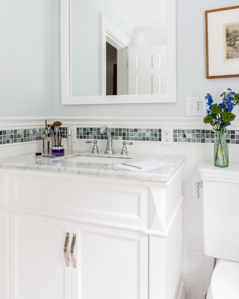 This is an example of a small traditional ensuite bathroom in Boston with white cabinets, a built-in bath, a shower/bath combination, a one-piece toilet, white tiles, porcelain tiles, blue walls, porcelain flooring, a submerged sink and marble worktops.