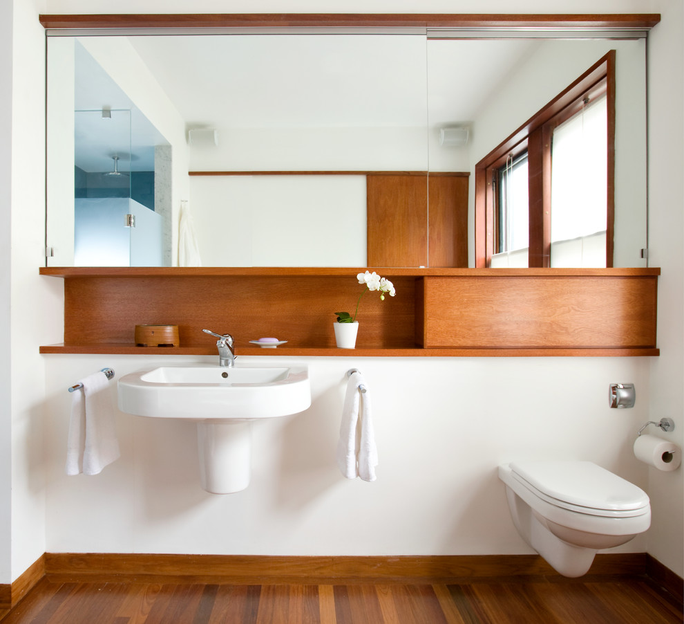 This is an example of a large contemporary ensuite bathroom in Boston with a wall-mounted sink, flat-panel cabinets, medium wood cabinets, a corner shower, a wall mounted toilet, white walls and medium hardwood flooring.