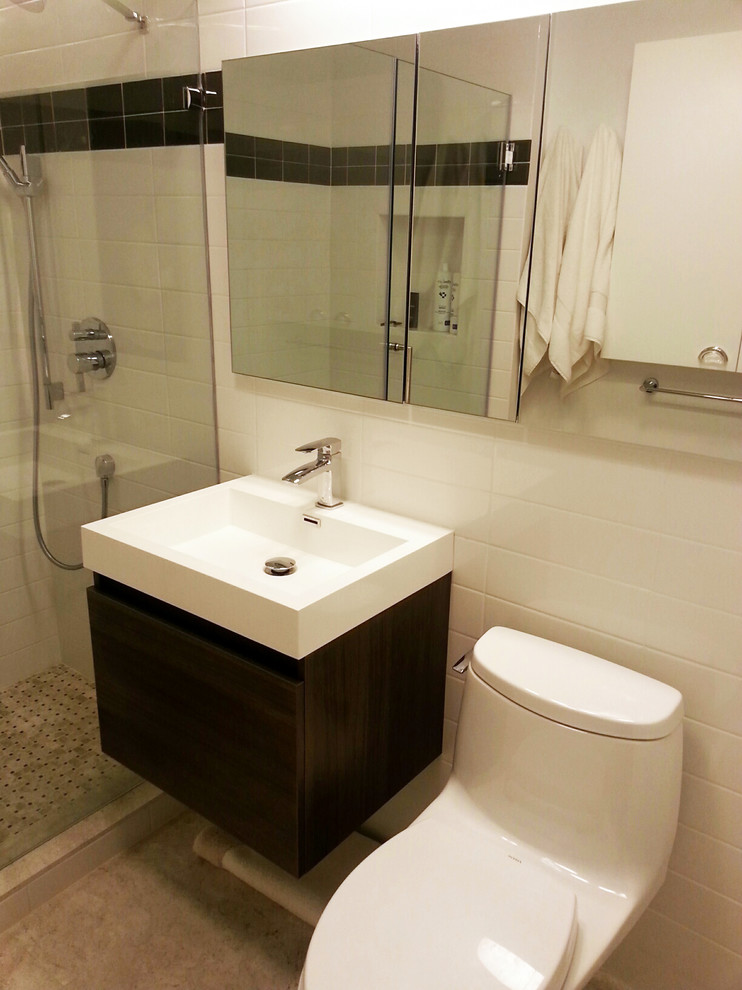 Inredning av ett modernt litet en-suite badrum, med ett integrerad handfat, släta luckor, skåp i mellenmörkt trä, bänkskiva i akrylsten, en dusch i en alkov, en toalettstol med hel cisternkåpa, flerfärgad kakel, glaskakel, vita väggar och kalkstensgolv