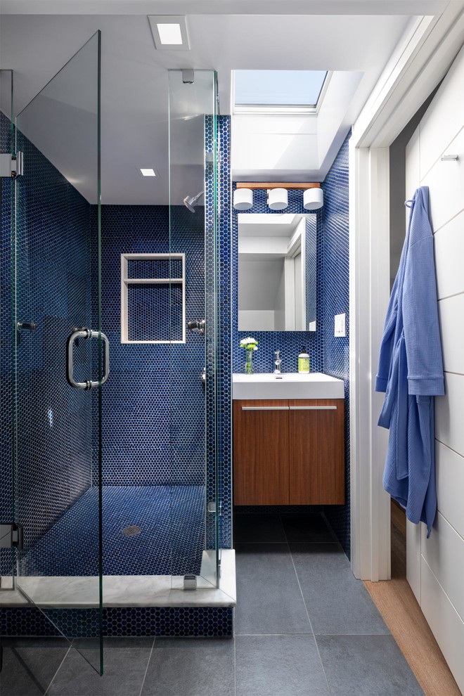 Ispirazione per una stanza da bagno con doccia design di medie dimensioni con ante lisce, ante in legno scuro, doccia alcova, piastrelle blu, piastrelle a mosaico, lavabo integrato, pavimento grigio, porta doccia a battente e top bianco