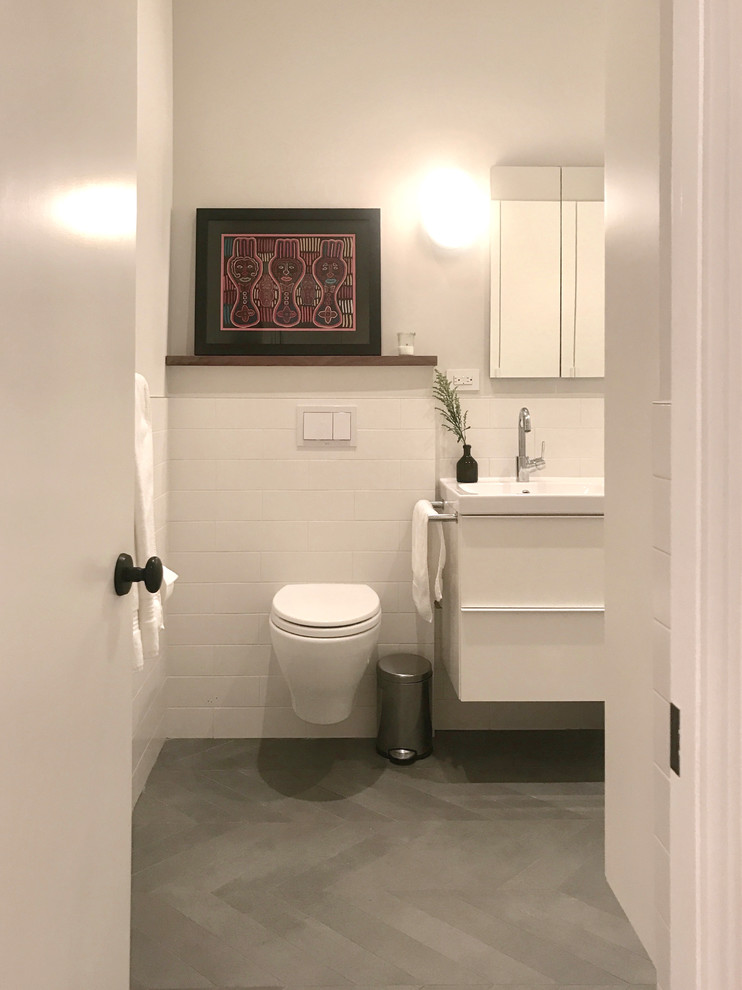 Kleines Modernes Badezimmer En Suite mit flächenbündigen Schrankfronten, weißen Schränken, Einbaubadewanne, Duschbadewanne, Wandtoilette, weißen Fliesen, Porzellanfliesen, weißer Wandfarbe, Porzellan-Bodenfliesen und Wandwaschbecken in New York
