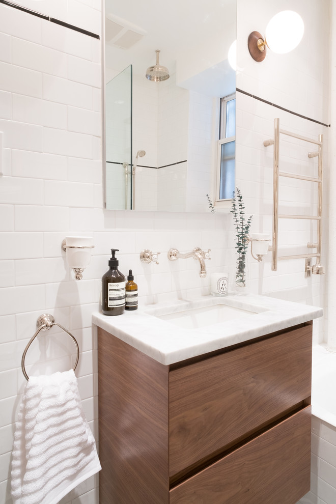 Idéer för att renovera ett litet funkis badrum med dusch, med släta luckor, skåp i mellenmörkt trä, ett badkar i en alkov, en dusch/badkar-kombination, vit kakel, tunnelbanekakel, vita väggar, ett undermonterad handfat, marmorbänkskiva, en toalettstol med separat cisternkåpa och klinkergolv i keramik