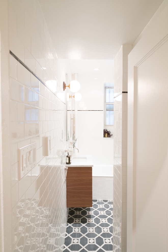 Idéer för att renovera ett litet funkis badrum med dusch, med släta luckor, skåp i mellenmörkt trä, ett badkar i en alkov, en dusch/badkar-kombination, en toalettstol med separat cisternkåpa, vit kakel, tunnelbanekakel, vita väggar, klinkergolv i keramik, ett undermonterad handfat och marmorbänkskiva