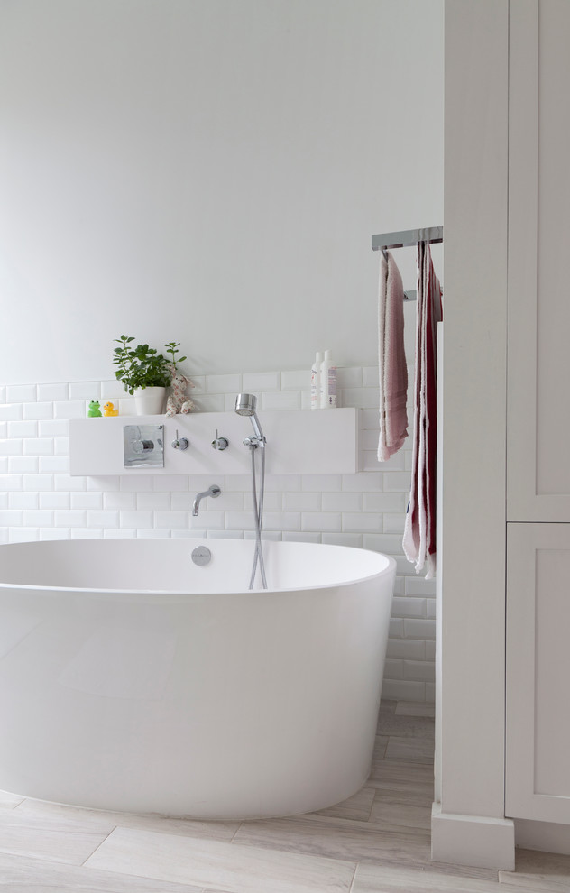 Inspiration for an industrial bathroom in New York with a freestanding bath, white tiles, white walls and light hardwood flooring.