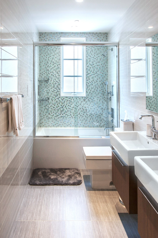 Modernes Badezimmer mit blauen Fliesen, Badewanne in Nische, Toilette mit Aufsatzspülkasten, integriertem Waschbecken, Duschbadewanne, Mosaikfliesen und dunklen Holzschränken in New York