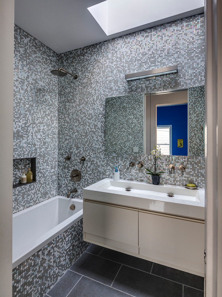 На фото: ванная комната в современном стиле с раковиной с несколькими смесителями, плоскими фасадами, белыми фасадами, ванной в нише, душем над ванной, плиткой мозаикой и разноцветной плиткой с