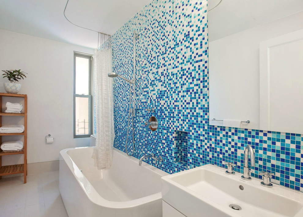 Cette image montre une salle de bain design avec un lavabo suspendu, une baignoire indépendante, un combiné douche/baignoire, un carrelage bleu, mosaïque et un mur blanc.