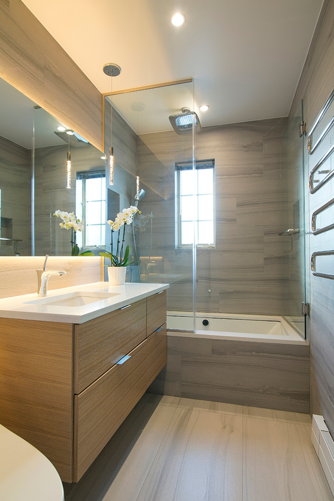 Photo of a medium sized contemporary ensuite half tiled bathroom in New York with flat-panel cabinets, light wood cabinets, an alcove bath, an alcove shower, grey tiles, porcelain tiles, grey walls, porcelain flooring, a submerged sink, solid surface worktops, beige floors and a hinged door.