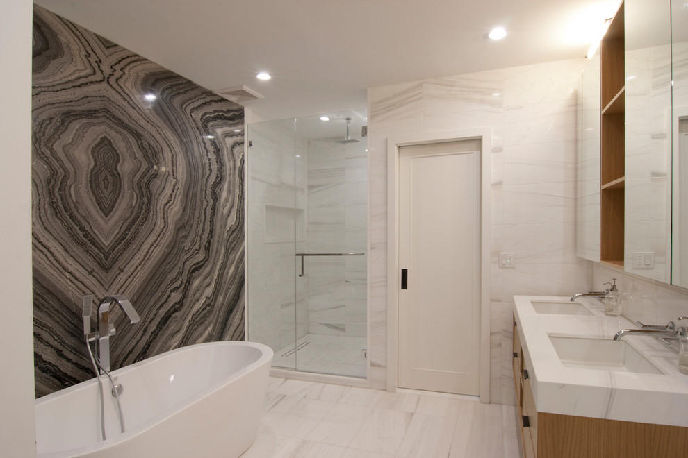 Large trendy master gray tile and stone slab porcelain tile and beige floor bathroom photo in New York with flat-panel cabinets, light wood cabinets, gray walls, an undermount sink, solid surface countertops, a hinged shower door and white countertops