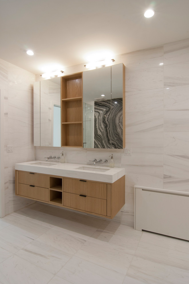 Inspiration for a large contemporary ensuite bathroom in New York with flat-panel cabinets, light wood cabinets, a freestanding bath, an alcove shower, grey tiles, stone slabs, grey walls, porcelain flooring, a submerged sink, solid surface worktops, beige floors, a hinged door and white worktops.