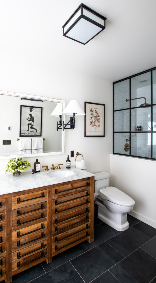 Classic bathroom in New York with medium wood cabinets, an alcove shower, white tiles, white walls, a submerged sink, black floors, white worktops and flat-panel cabinets.