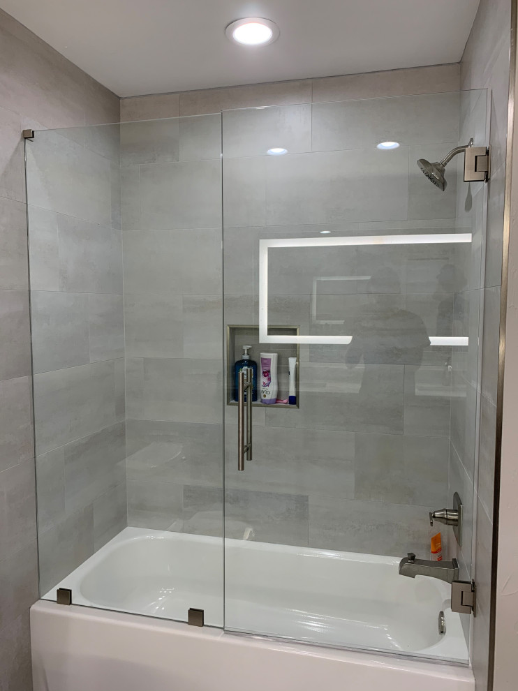 This is an example of a medium sized modern ensuite bathroom in Jacksonville with shaker cabinets, grey cabinets, an alcove bath, a shower/bath combination, a two-piece toilet, grey tiles, porcelain tiles, grey walls, porcelain flooring, a submerged sink, quartz worktops, grey floors, a hinged door, grey worktops, a wall niche, double sinks and a built in vanity unit.