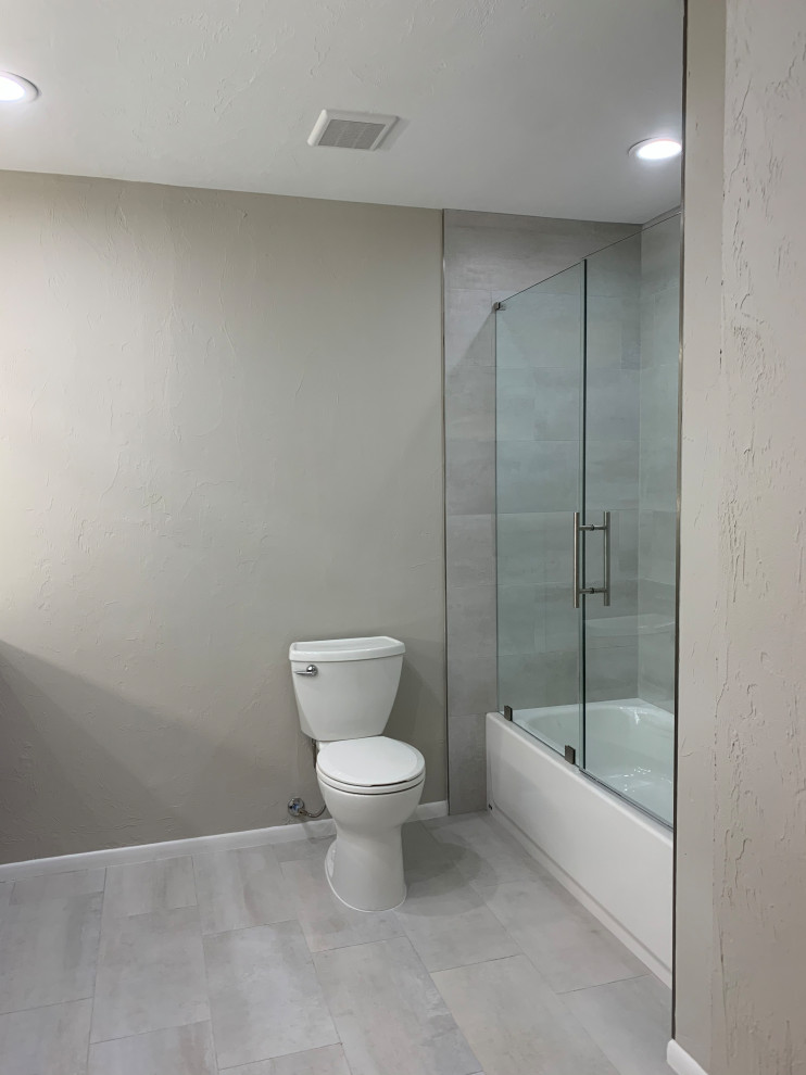 Idéer för att renovera ett mellanstort funkis grå grått en-suite badrum, med skåp i shakerstil, grå skåp, ett badkar i en alkov, en dusch/badkar-kombination, en toalettstol med separat cisternkåpa, grå kakel, porslinskakel, grå väggar, klinkergolv i porslin, ett undermonterad handfat, bänkskiva i kvartsit, grått golv och dusch med gångjärnsdörr