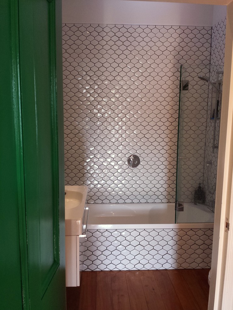 Kleines Modernes Badezimmer En Suite mit Wandwaschbecken, flächenbündigen Schrankfronten, weißen Schränken, Einbaubadewanne, Duschbadewanne, Toilette mit Aufsatzspülkasten, weißen Fliesen, Porzellanfliesen, weißer Wandfarbe und braunem Holzboden in Auckland