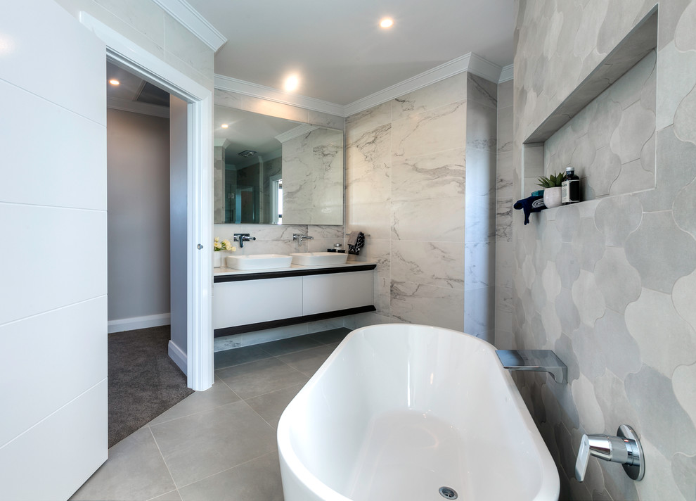 Modern inredning av ett en-suite badrum, med släta luckor, vita skåp, ett fristående badkar, grå kakel och ett fristående handfat