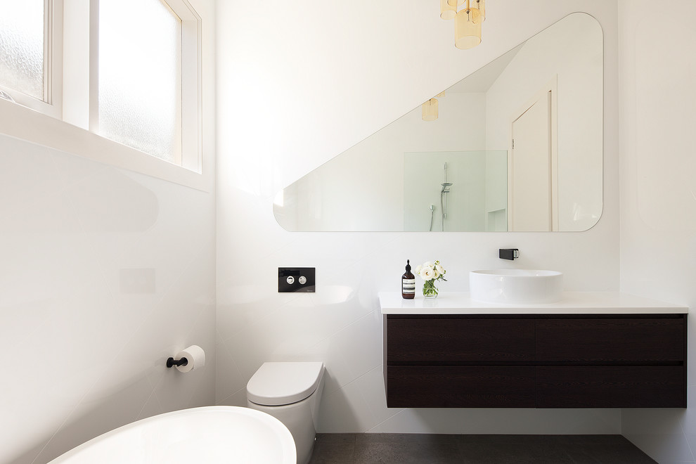 Photo of a large contemporary ensuite bathroom in Melbourne with raised-panel cabinets, dark wood cabinets, a freestanding bath, a walk-in shower, a wall mounted toilet, cement tiles, a vessel sink, solid surface worktops and white worktops.