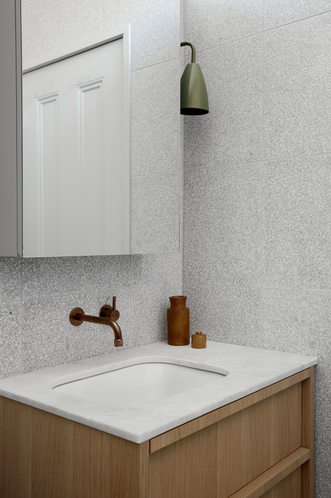 Exemple d'une salle de bain moderne en bois clair avec un placard à porte plane, un carrelage gris, un lavabo encastré, un plan de toilette blanc et meuble simple vasque.