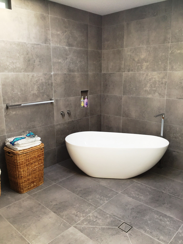 This is an example of a small modern ensuite bathroom in Sydney with freestanding cabinets, white cabinets, a freestanding bath, a double shower, a wall mounted toilet, grey tiles, slate tiles, grey walls, slate flooring, a built-in sink, limestone worktops, grey floors, an open shower and white worktops.