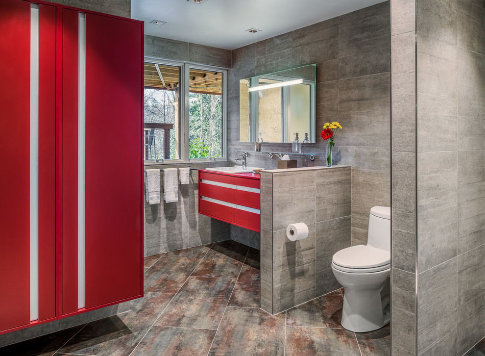 Modern inredning av ett badrum, med keramikplattor, ett nedsänkt handfat, släta luckor, röda skåp och grå kakel