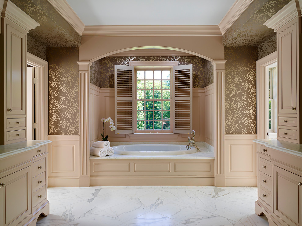 Cette image montre une douche en alcôve traditionnelle avec un placard avec porte à panneau surélevé, des portes de placard beiges, une baignoire posée, un lavabo encastré, un plan de toilette en marbre, WC séparés, un carrelage blanc, un mur marron et un sol en marbre.
