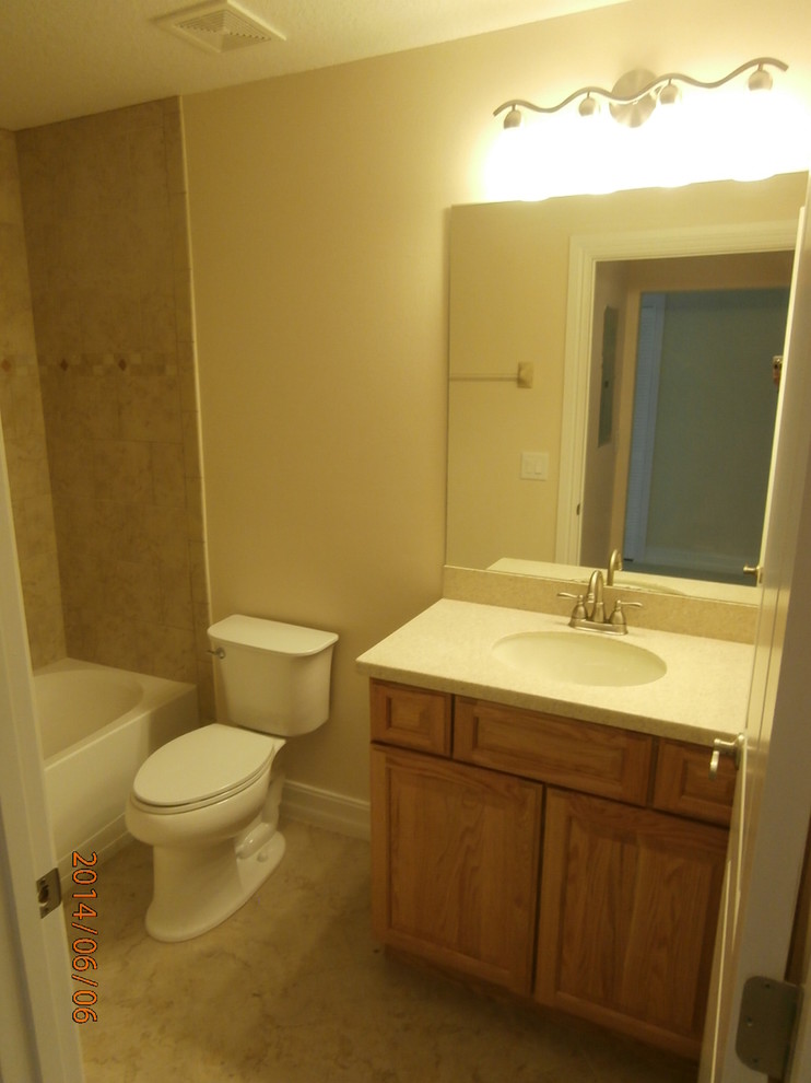 This is an example of a medium sized classic family bathroom in Orlando with a submerged sink, recessed-panel cabinets, light wood cabinets, solid surface worktops, a freestanding bath, a shower/bath combination, a two-piece toilet, beige tiles, porcelain tiles, beige walls and porcelain flooring.