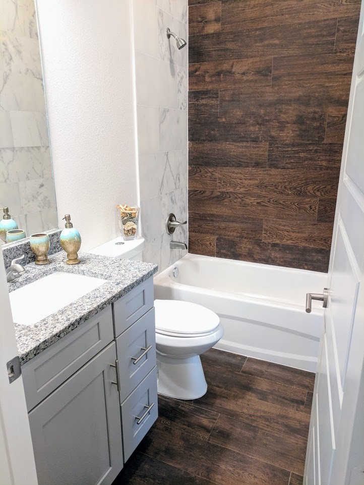 Inspiration for a medium sized contemporary family bathroom with recessed-panel cabinets, grey cabinets, a built-in bath, a shower/bath combination, a one-piece toilet, white tiles, marble tiles, white walls, porcelain flooring, a submerged sink, granite worktops, brown floors, a shower curtain and grey worktops.
