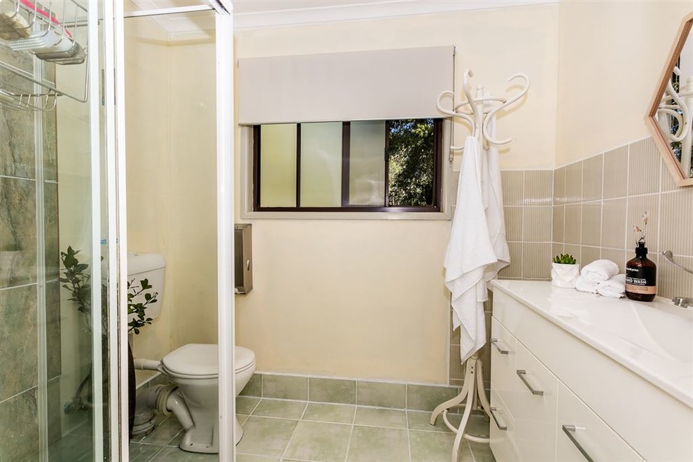 Photo of a small ensuite bathroom in Brisbane with a corner shower, beige tiles, ceramic tiles, ceramic flooring, an integrated sink, green floors and a sliding door.