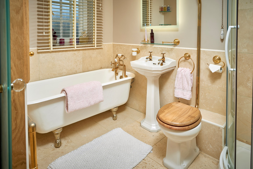 Foto på ett mellanstort vintage badrum för barn, med ett badkar med tassar, en hörndusch, en toalettstol med separat cisternkåpa, travertinkakel, beige väggar, travertin golv, ett piedestal handfat och dusch med skjutdörr