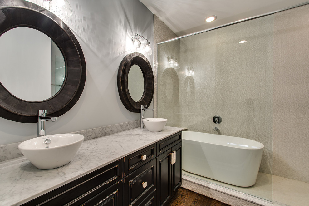 Photo of a medium sized classic shower room bathroom in Chicago with recessed-panel cabinets, distressed cabinets, a freestanding bath, an alcove shower, grey tiles, pebble tiles, beige walls, medium hardwood flooring, a vessel sink, marble worktops, brown floors and a hinged door.