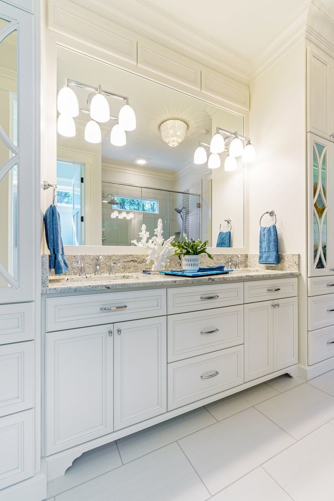 Example of a large master porcelain tile and white floor corner shower design in Other with louvered cabinets, white cabinets, white walls, an undermount sink, granite countertops, a hinged shower door and multicolored countertops