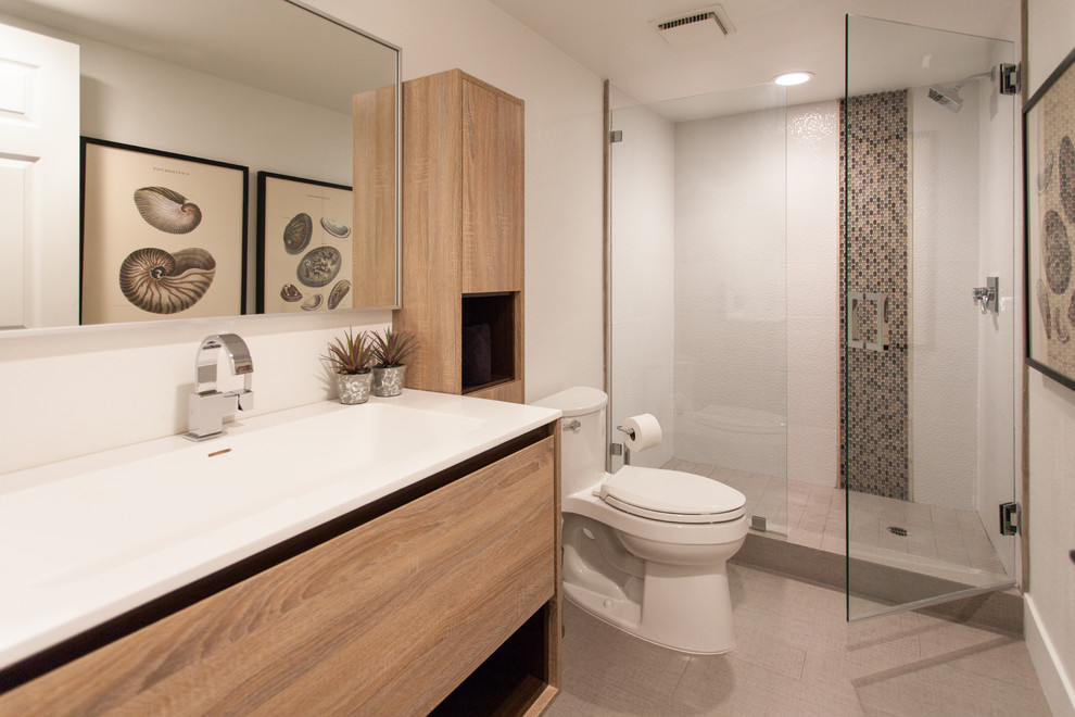 Example of a mid-sized trendy 3/4 beige tile and mosaic tile ceramic tile alcove shower design in Orange County with flat-panel cabinets, light wood cabinets, a one-piece toilet, white walls, a trough sink and solid surface countertops