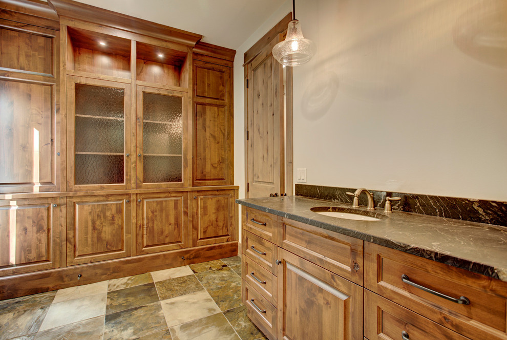 Réalisation d'une grande salle de bain principale chalet en bois foncé avec un placard avec porte à panneau surélevé, un mur marron, un lavabo encastré et un sol marron.