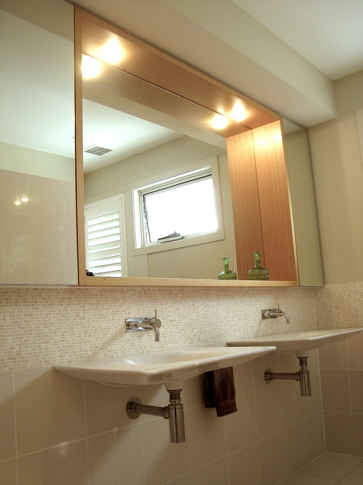 Imagen de cuarto de baño actual con lavabo suspendido, puertas de armario de madera clara, bañera encastrada, ducha abierta, sanitario de pared y baldosas y/o azulejos beige