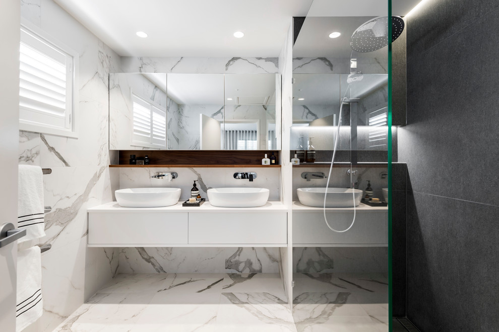 Modern inredning av ett vit vitt badrum, med släta luckor, vita skåp, vit kakel, vita väggar, ett fristående handfat och vitt golv