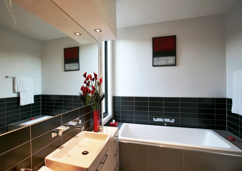 Photo of a medium sized modern family bathroom in Melbourne with flat-panel cabinets, white cabinets, a built-in bath, a built-in shower, a one-piece toilet, black tiles, ceramic tiles, white walls, porcelain flooring, a console sink, engineered stone worktops, grey floors and a hinged door.
